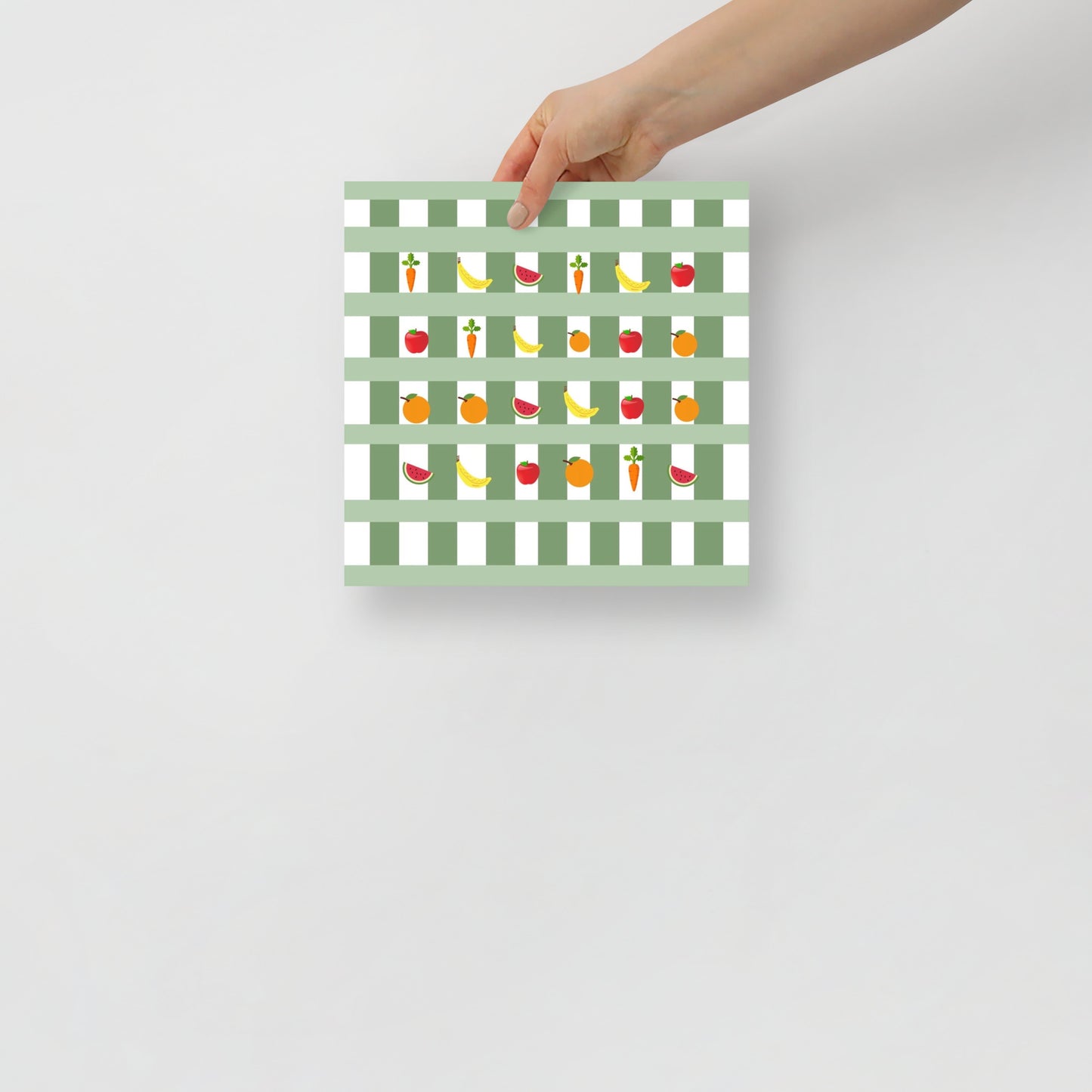 Hand holding a green and white gingham pattern with colourful fruit illustrations on a light gray background