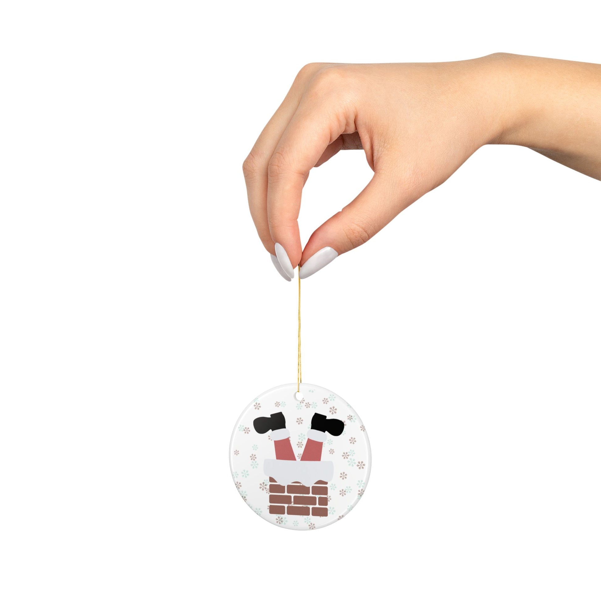 Hand holding a round ornament with a cartoon santa boots in chimney design on a white background