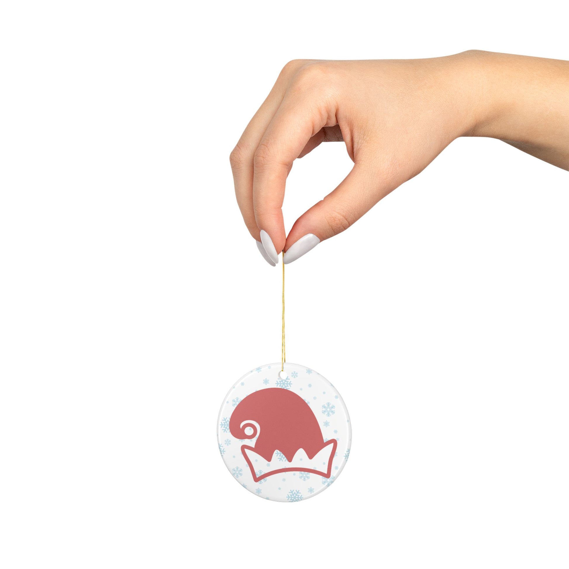 Hand holding a round ornament with a red and white elf hat design on a white background with blue snowflakes