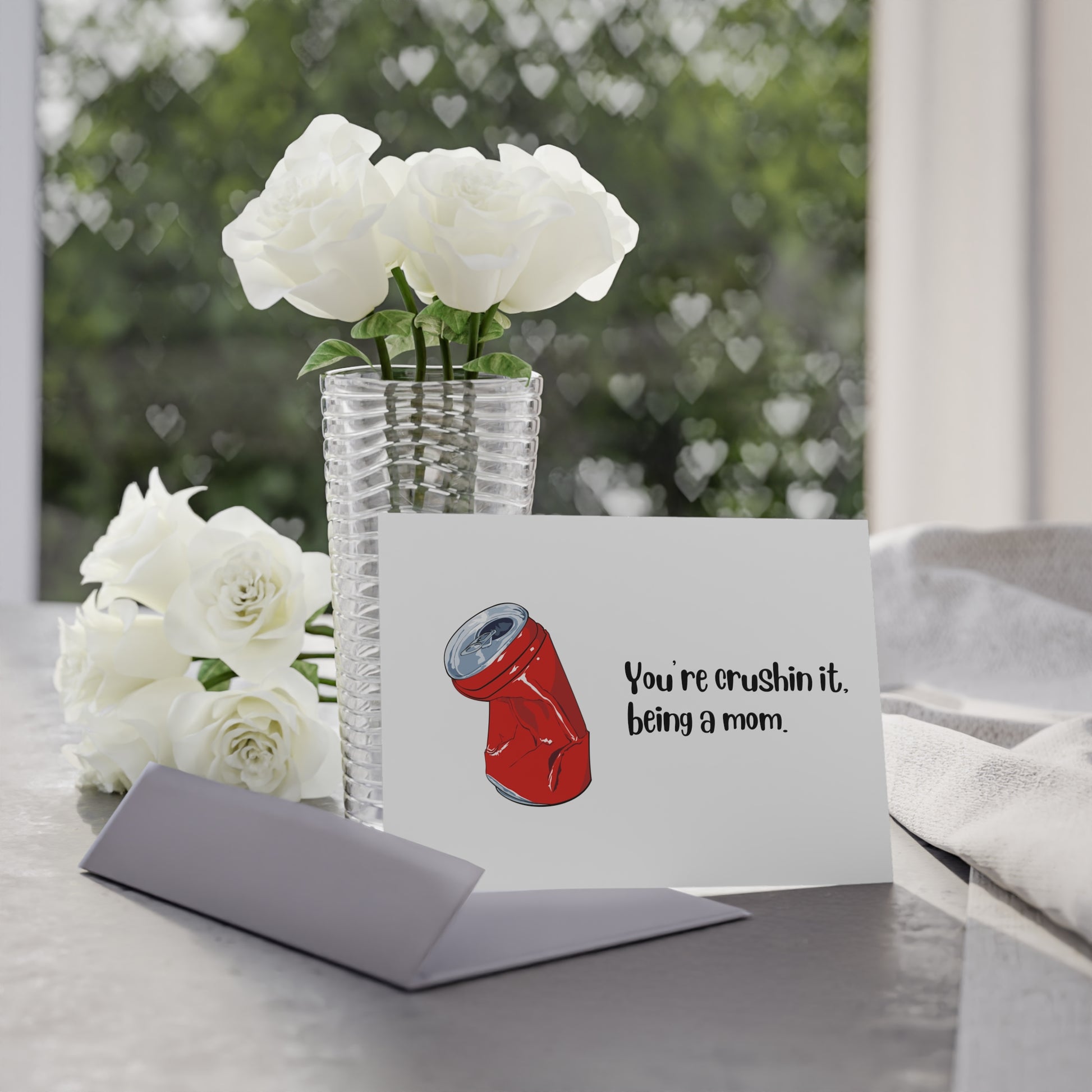 Greeting card with a red can illustration and text, placed on a table with flowers in the background.