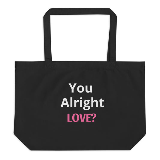 A black tote bag on a white background with "You Alright Love?" text written in white and pink on the bag