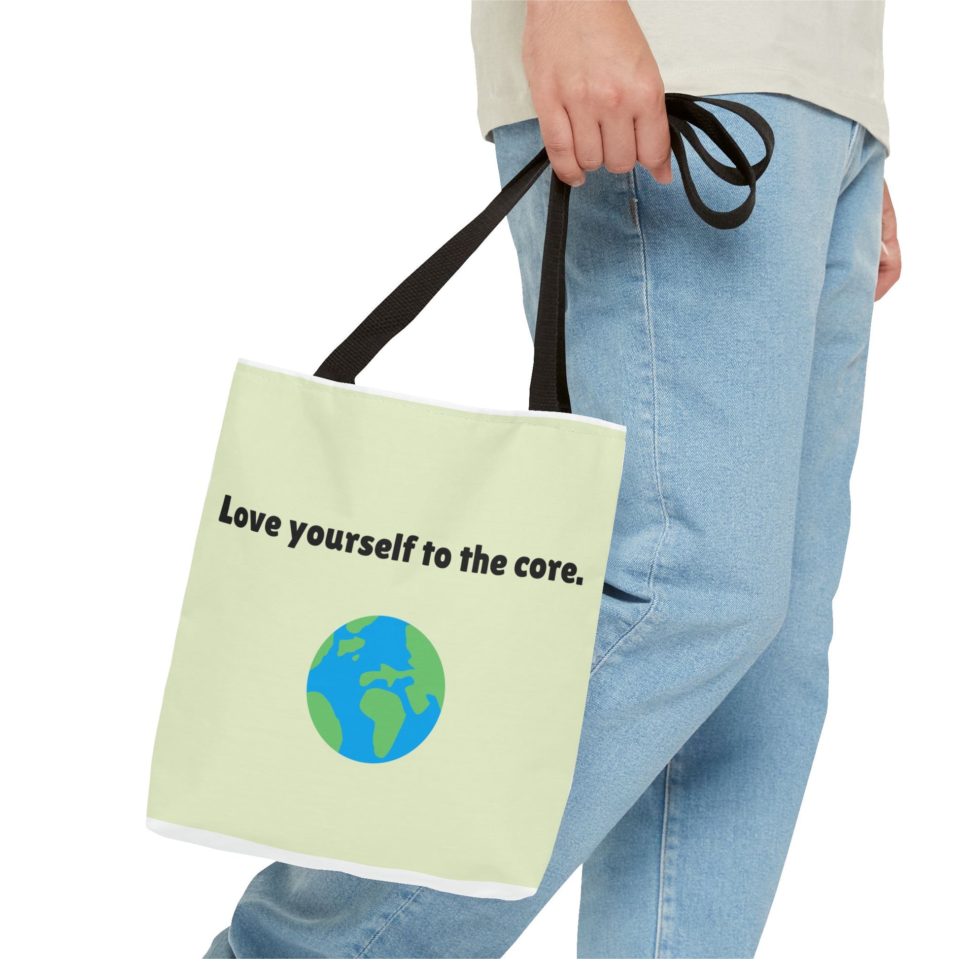 Tote bag with 'Love yourself to the core.' text and Earth graphic held by a person wearing jeans.