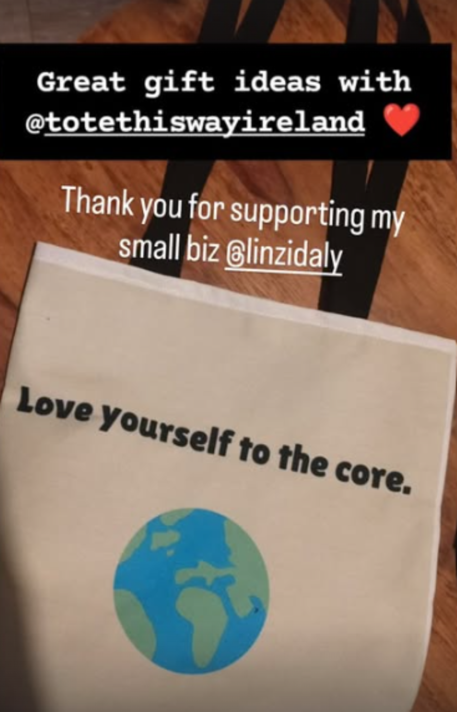 A cream canvas tote bag with black handles, featuring the printed text 'Love yourself to the core.' and a blue and green globe graphic.