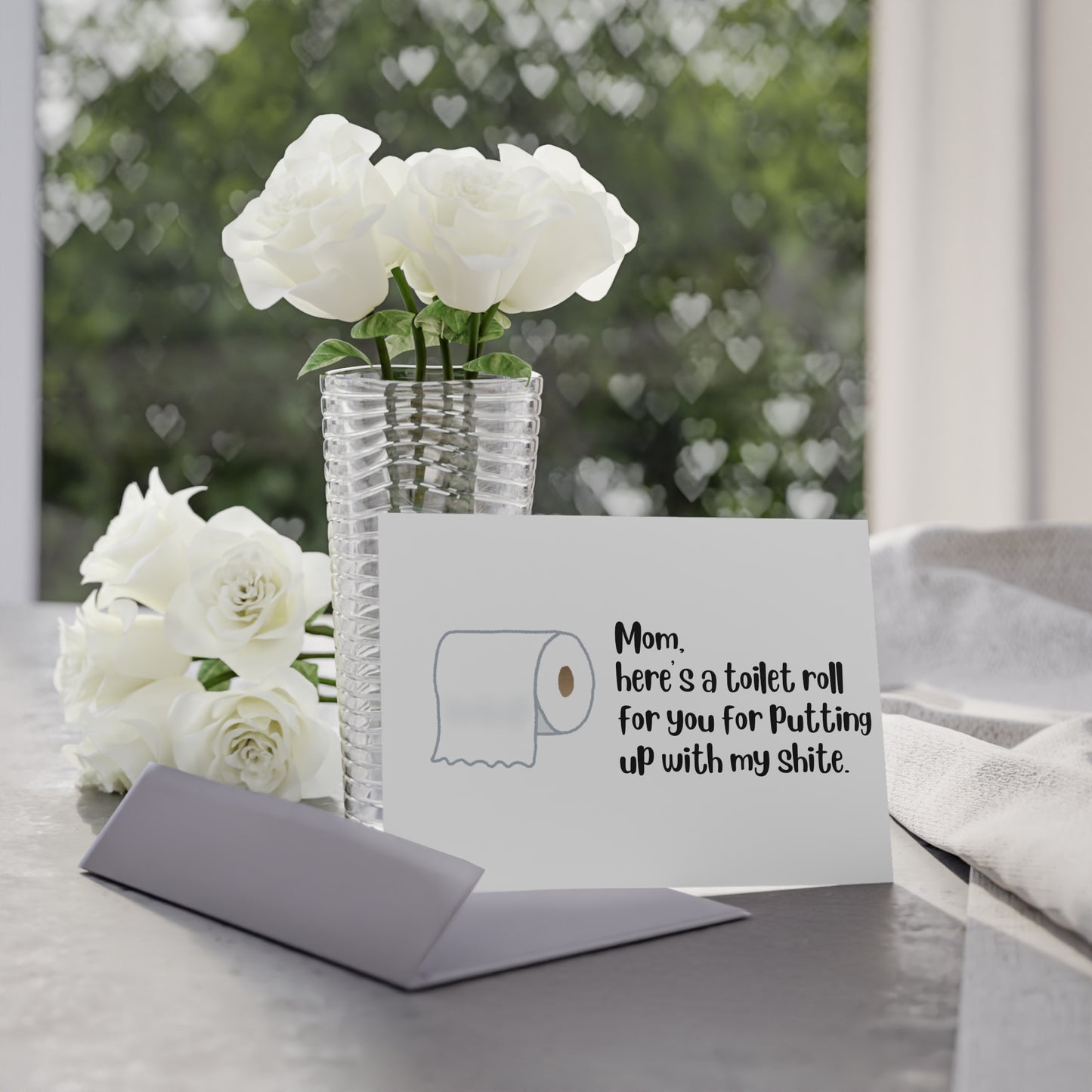 Card with humorous message and toilet paper roll illustration next to white flowers on a table.