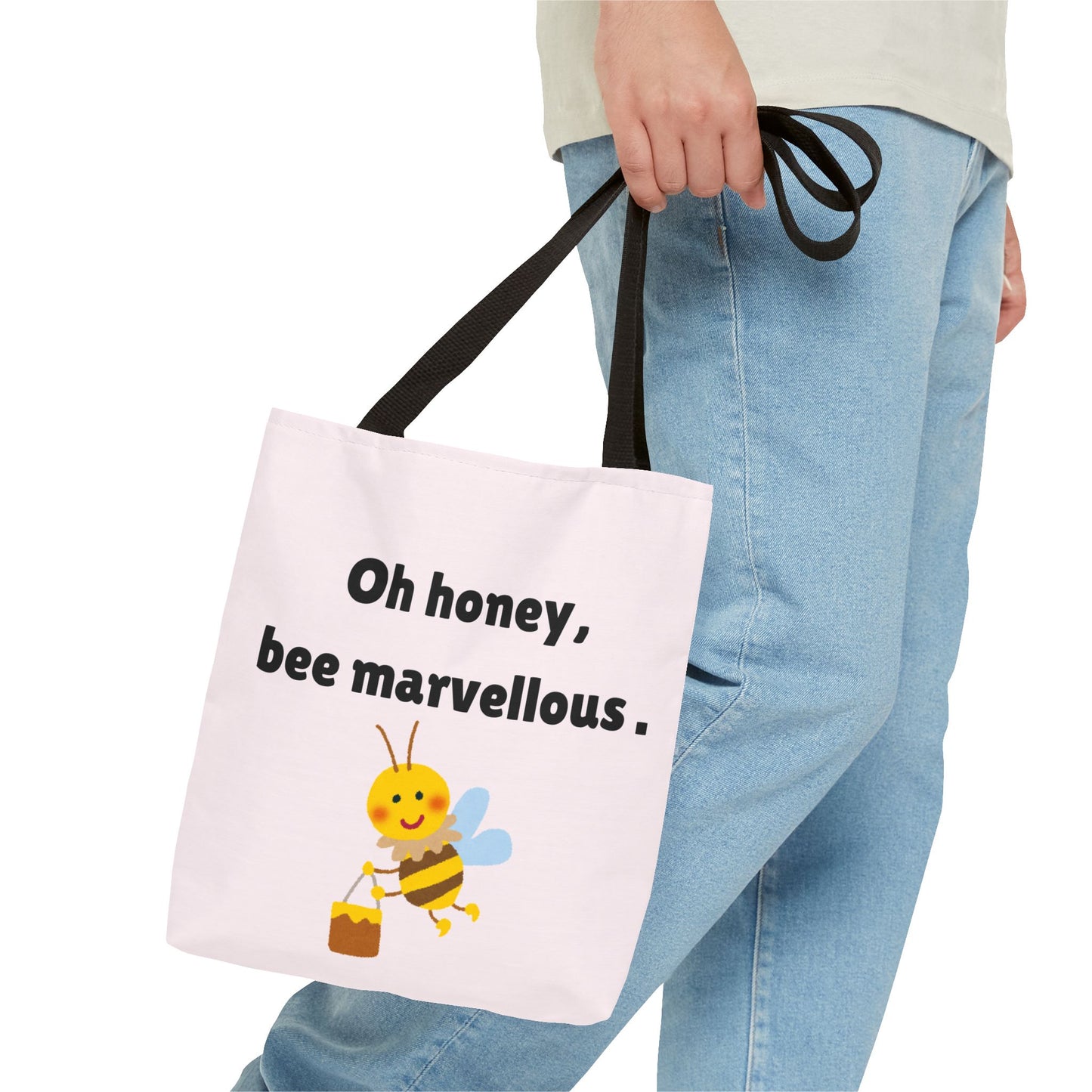 Tote bag with a bee design and text held by a person wearing jeans.