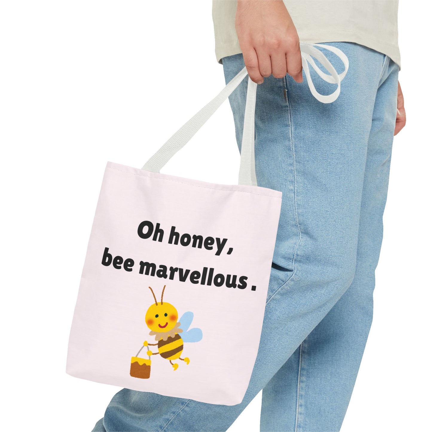 Tote bag with a bee design and text held by a person wearing jeans.